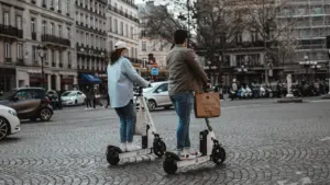 Deux personnes circulant sur des trottinettes électriques dans une rue pavée française.