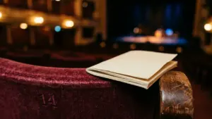 Un programme de théâtre plié repose sur un siège en velours rouge numéroté quatorze.
