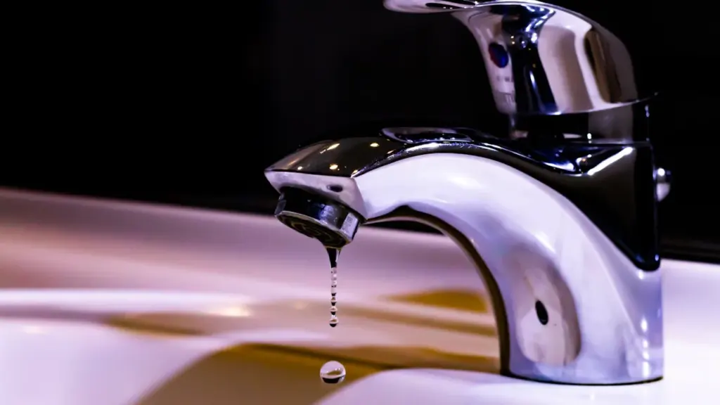 Gros plan sur un robinet avec une goutte d'eau tombant lentement dans un évier.