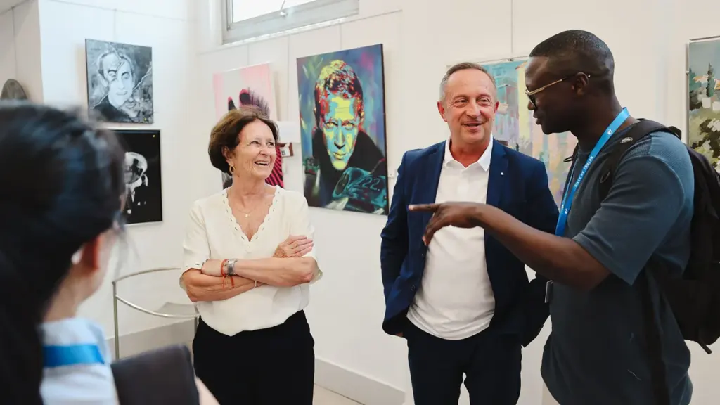 Trois personnes discutent joyeusement dans une galerie d'art entourées de plusieurs peintures colorées.