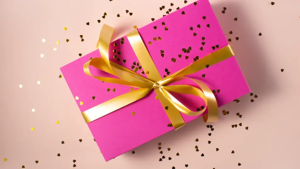 Cadeau emballé dans du papier rose avec un ruban doré brillant.