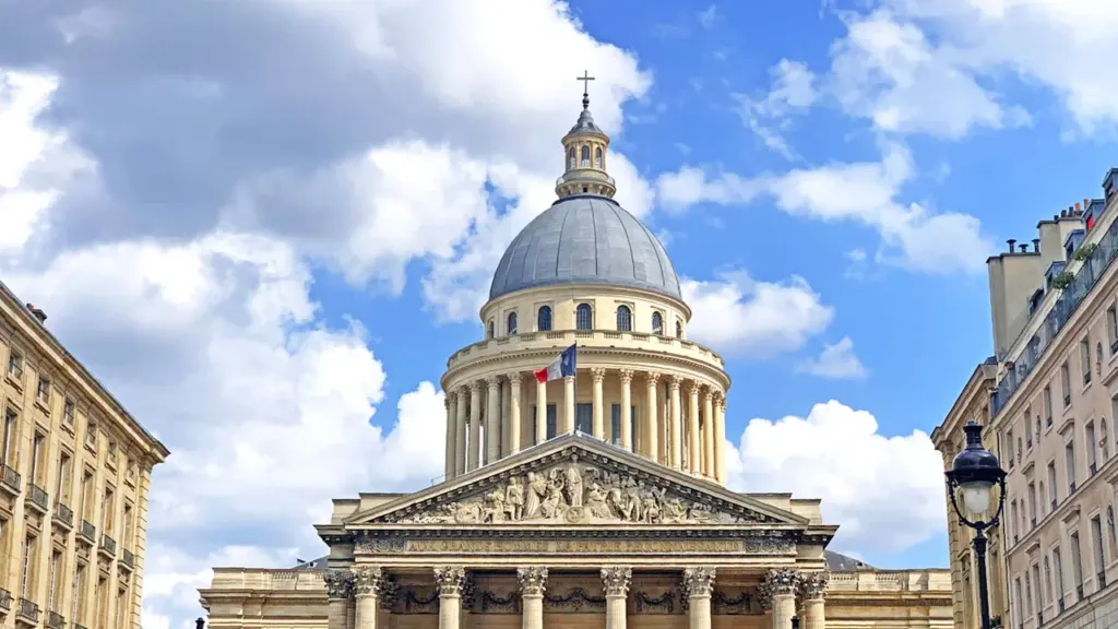 Vue emblématique du Panthéon à Paris sous un ciel bleu avec drapeau français.