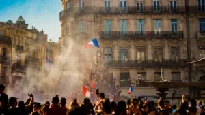 Foule en liesse brandissant le drapeau français devant des bâtiments haussmanniens historiques.