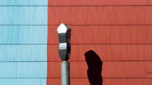 Un horodateur urbain placé devant un mur coloré bicolore, rouge et bleu.