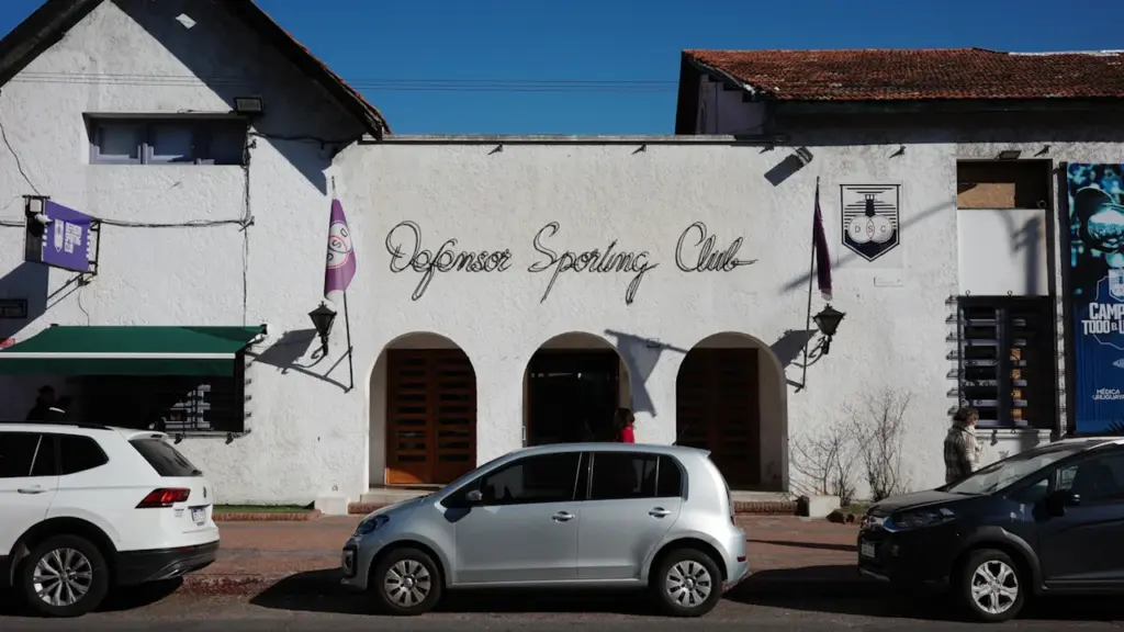 Façade d'un bâtiment sportif urbain avec des voitures garées devant sur une rue ensoleillée.