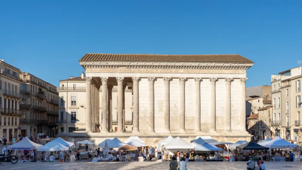 Le temple romain antique Maison Carrée à Nîmes avec un marché artisanal devant lui.