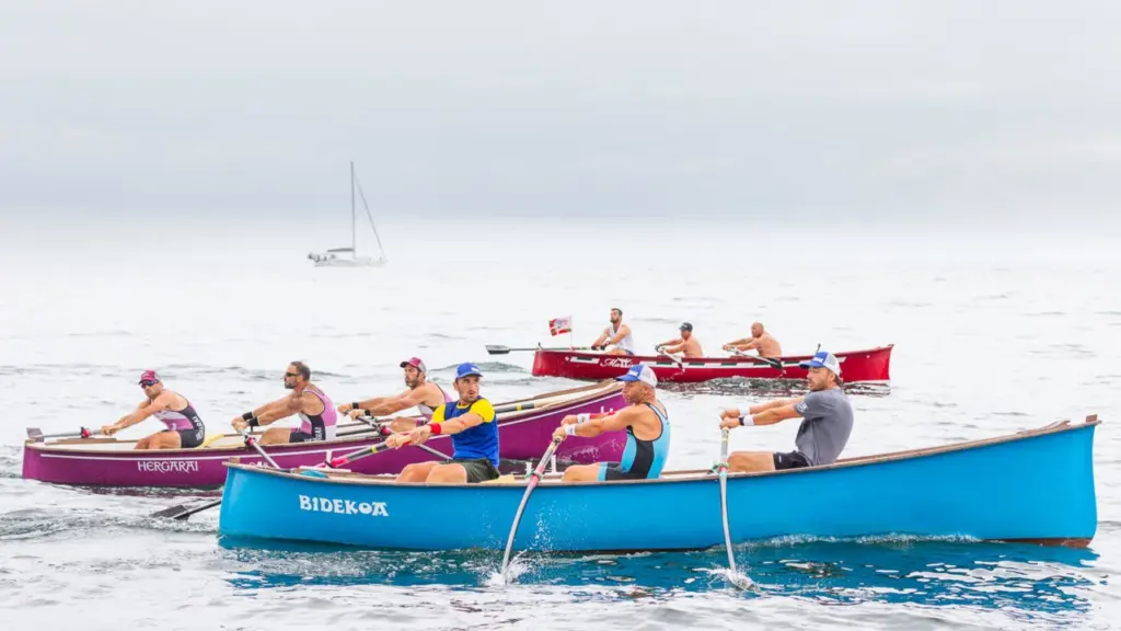 Plusieurs équipes d'hommes rament avec intensité dans des barques traditionnelles colorées sur l'océan.