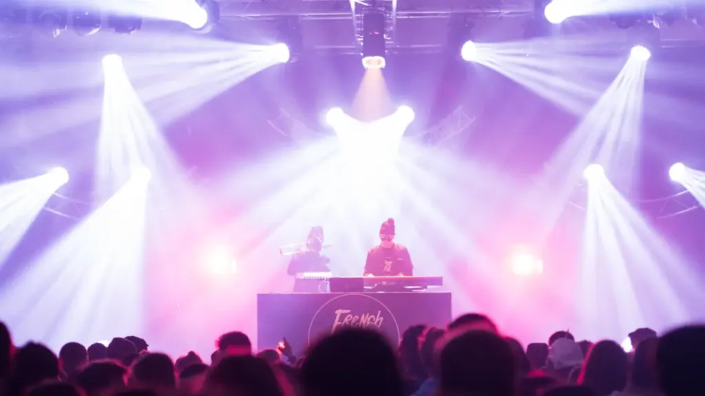 DJ en concert devant une foule sur une scène avec des jeux de lumière.