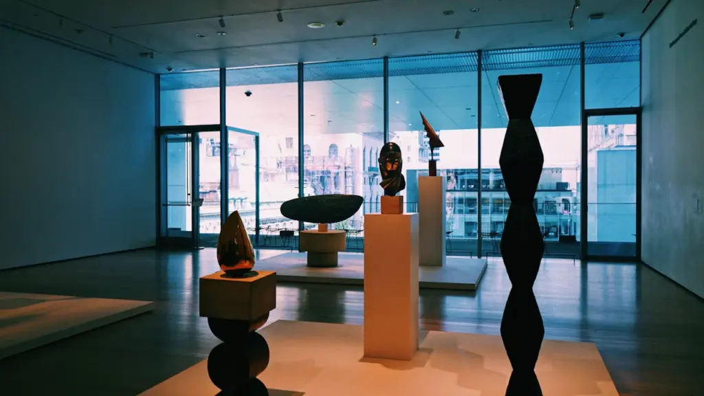 Galerie d'art contemporain lumineuse avec des sculptures sur des socles centraux.