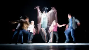 Groupe de danseurs contemporains effectuant une chorégraphie sur une scène sombre et éclairée.