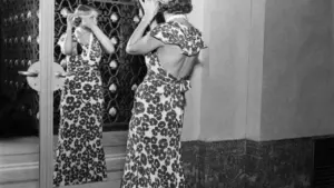Une femme en robe longue fleurie s'ajuste les cheveux devant un grand miroir mural.